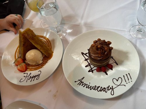 A dessert plate with a slice of cake and ice cream, decorated with "Happy" and "Anniversary" in chocolate sauce.