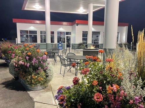A brightly lit outdoor seating area with colorful flowers and plants, next to a modern building at night.