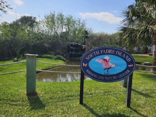 Sign for South Padre Island Birding and Nature Center, with a pond and lush greenery in the background.