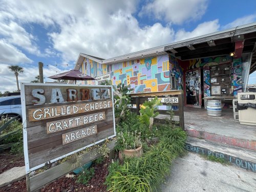 Colorful exterior of Sarbez, a grilled cheese and craft beer arcade, featuring a vibrant mural and outdoor seating.