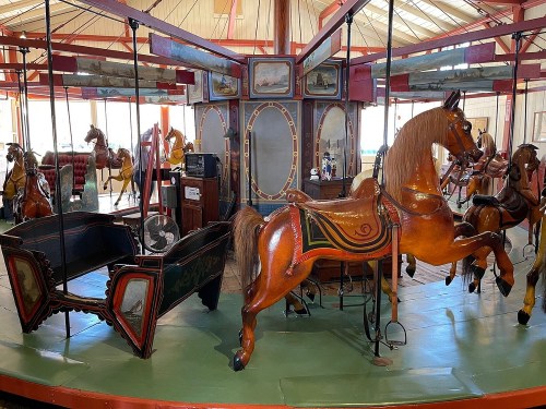 A vintage carousel featuring intricately carved wooden horses and a decorative platform in a bright indoor setting.