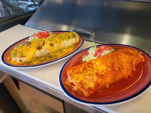 Two plates of enchiladas: one with green sauce and cheese, the other with red sauce, topped with lettuce and tomatoes.