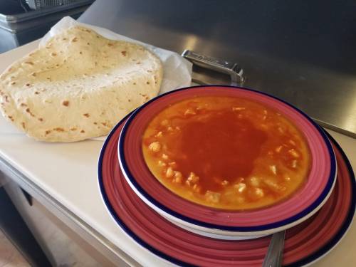 A bowl of orange soup with chunks, served with a side of flatbread on a plate.