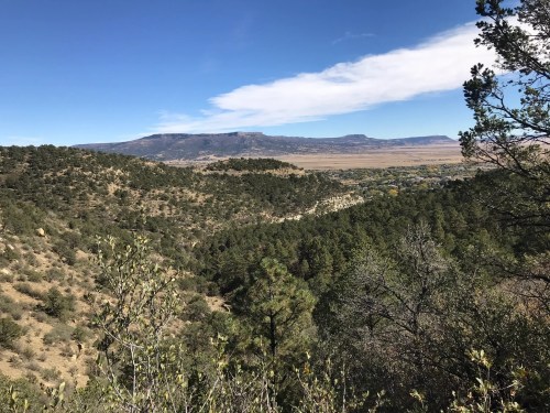 A scenic view of rolling hills and mountains under a clear blue sky, surrounded by lush greenery.