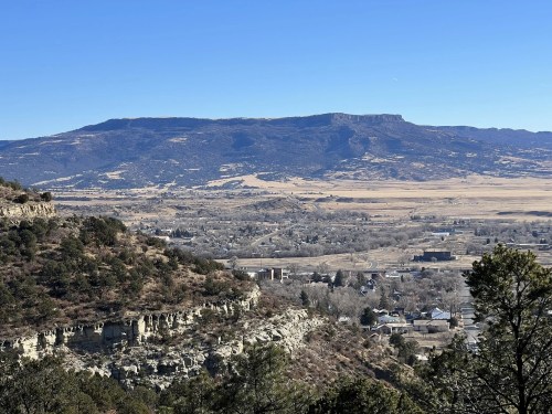 A panoramic view of a valley with mountains in the background, featuring a mix of trees and open fields.