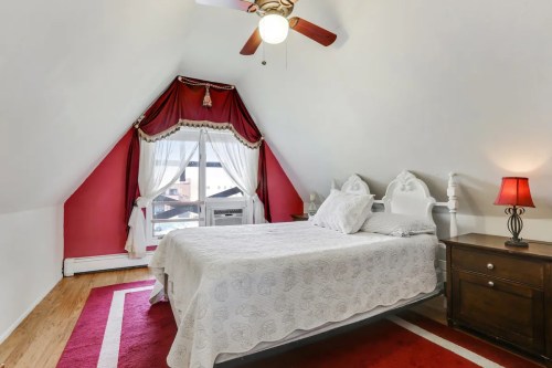 Cozy bedroom with sloped ceiling, red accents, a large window, and a bedside lamp.
