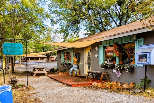 Charming bakery with a rustic exterior, colorful windows, and a welcoming porch surrounded by trees.