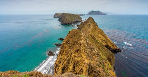 A scenic view of rugged coastal cliffs and islands, with turquoise waters and a cloudy sky in the background.