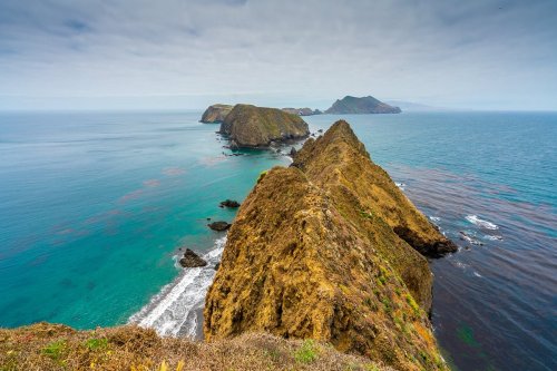 A scenic view of rugged coastal cliffs meeting the turquoise ocean under a cloudy sky.