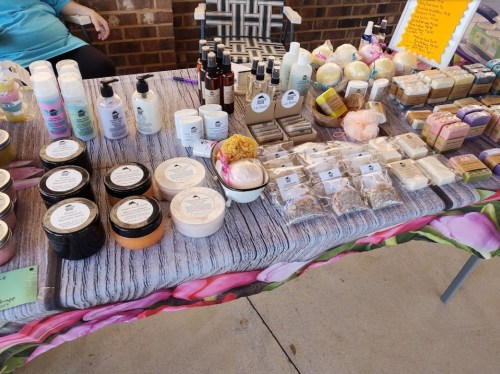 A market table displaying various handmade soaps, lotions, and beauty products in colorful packaging.