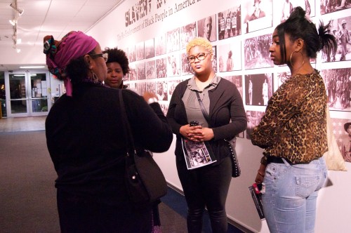 Four women engage in conversation in an art gallery, surrounded by black-and-white photographs depicting Black history.