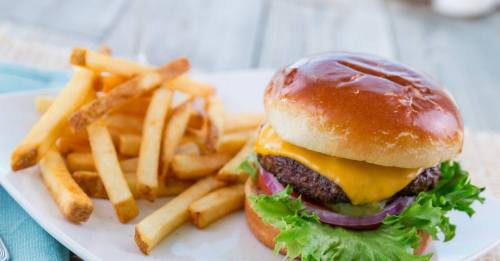 A juicy cheeseburger with lettuce, tomato, and onion, served with a side of golden French fries on a white plate.