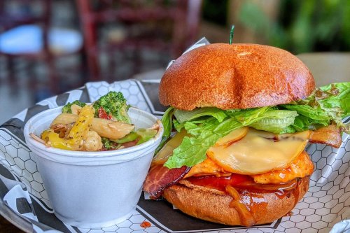 A delicious burger with lettuce, cheese, and bacon, served with a side of mixed vegetables in a cup.