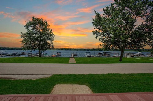 Scenic view of a lake at sunset, with boats docked and trees lining the shore, framed by a grassy area and pathway.