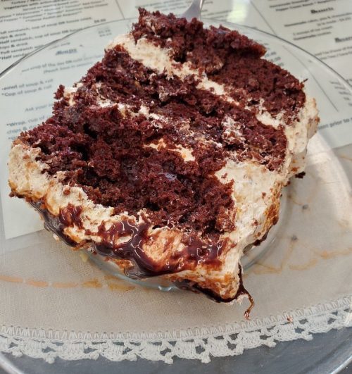 A slice of chocolate cake with layers of cream and chocolate drizzle on a glass plate.