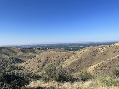 A panoramic view of rolling hills under a clear blue sky, with a distant city visible in the valley below.