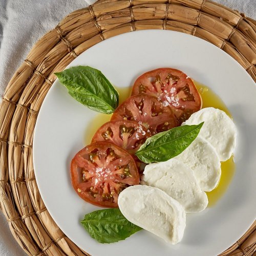 Sliced tomatoes and fresh mozzarella on a plate, garnished with basil leaves and drizzled with olive oil.