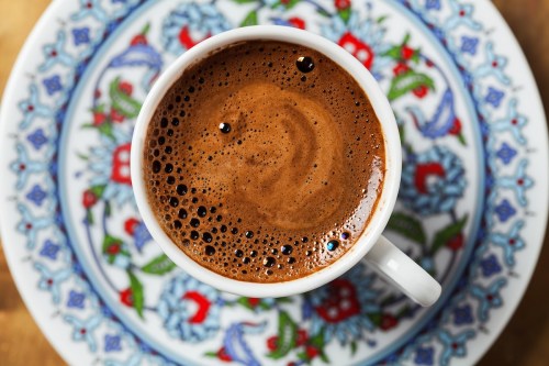 A close-up of a cup of coffee with frothy surface, placed on a decorative patterned plate.