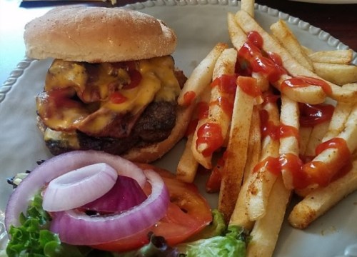 A cheeseburger with melted cheese, lettuce, tomato, and onion, served with fries drizzled with ketchup.