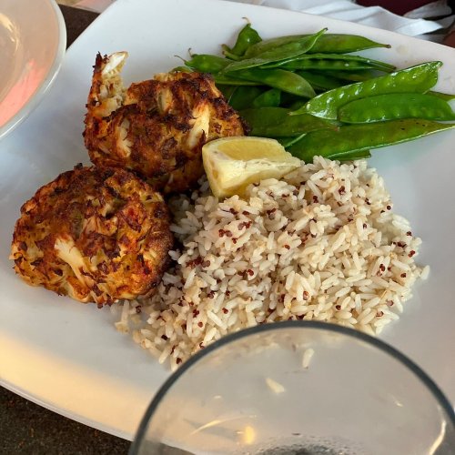 A plate featuring two crab cakes, rice, snap peas, and a lemon wedge.