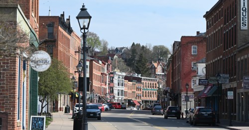 A charming street lined with historic brick buildings, shops, and trees under a clear blue sky.