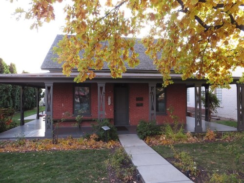 A charming brick house with a porch, surrounded by autumn leaves and a well-maintained garden.