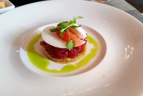 A gourmet dish featuring layered tuna tartare, garnished with radish, herbs, and a drizzle of green sauce on a white plate.