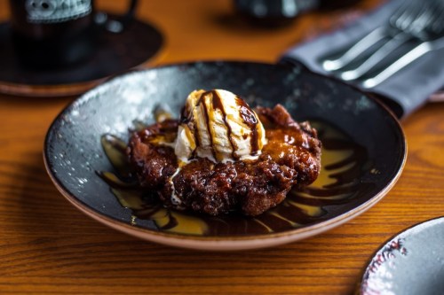 A warm dessert featuring a chocolate brownie topped with vanilla ice cream and drizzled with chocolate sauce on a plate.