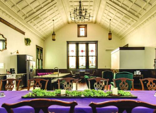 A spacious room with high ceilings, stained glass windows, and a long table set with greenery and candles.