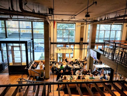 A bustling restaurant interior with large windows, filled with diners at tables and a modern design.