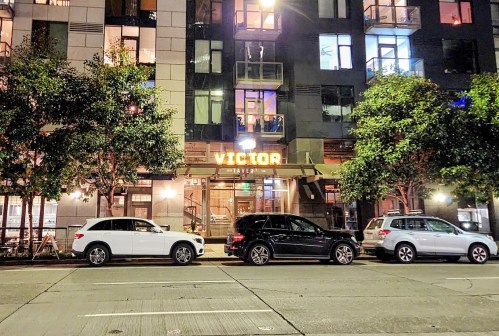 A street view of a building with the illuminated sign "VICTOR" and parked cars in front at night.