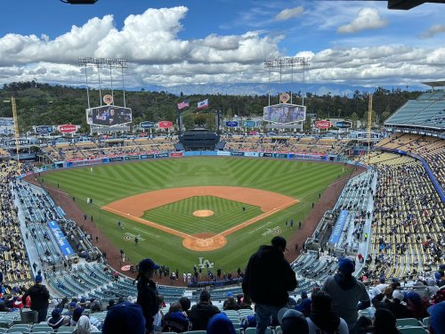 A panoramic view of a baseball stadium with a well-maintained field, empty seats, and cloudy skies above.