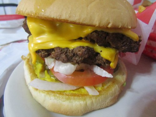 A close-up of a cheeseburger with two layers of melted cheese, lettuce, tomato, and onions on a soft bun.