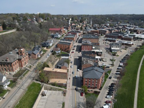 Aerial view of a small town with historic buildings, streets, and greenery in the background.
