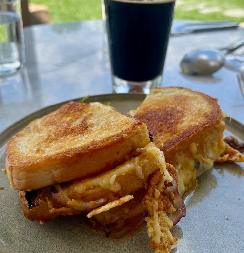 A grilled cheese sandwich with crispy edges, served on a plate with a dark beverage in the background.