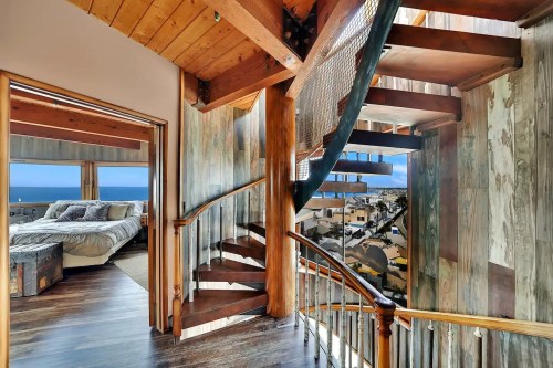 A spiral staircase leads to a bright, open space with ocean views and wooden accents in a modern home.