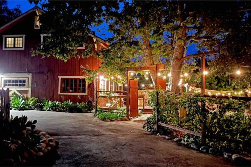 A cozy red house at night, illuminated by warm lights, surrounded by greenery and a welcoming pathway.