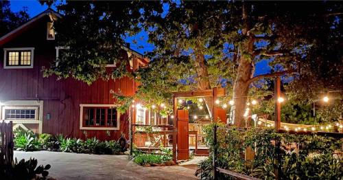 A cozy red barn-style house illuminated by string lights at night, surrounded by greenery and a welcoming entrance.