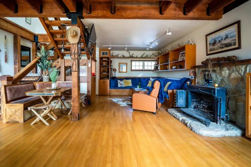 Cozy living space with wooden beams, a stone fireplace, seating area, and a dining table, featuring warm, inviting decor.