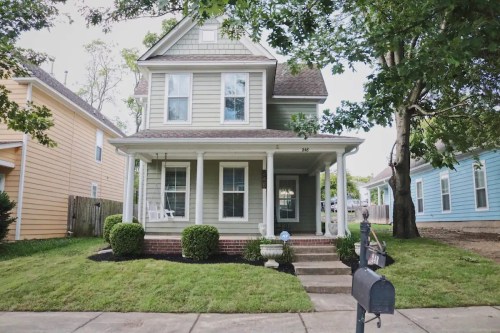 A charming two-story house with a front porch, surrounded by greenery and a well-maintained lawn.
