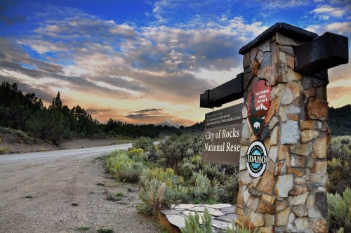 Sign for City of Rocks National Reserve in Idaho, with a scenic sky and dirt road in the background.