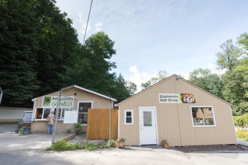 A small zoo entrance with a gift shop, surrounded by trees and a clear blue sky.
