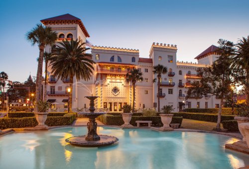 Historic building with ornate architecture, surrounded by palm trees and a fountain, at dusk.