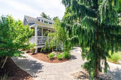 A charming house with a porch surrounded by lush greenery and a stone pathway.