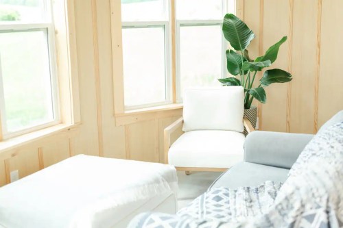 Bright, airy room with large windows, a light chair, a gray sofa, and a potted plant in the corner.