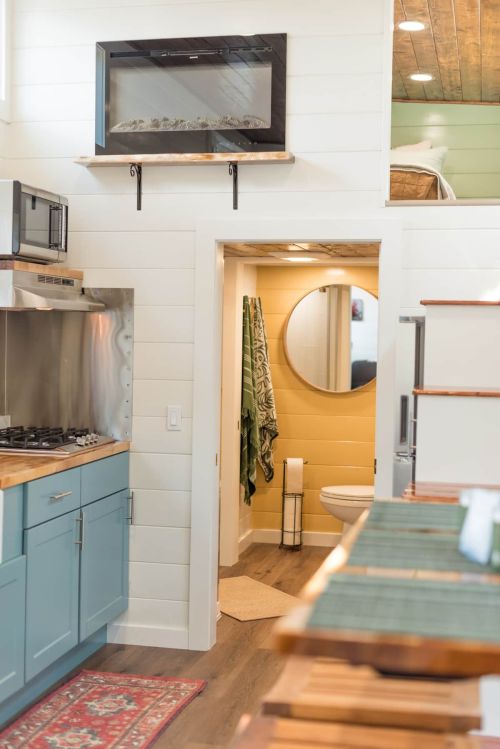 Cozy tiny home interior featuring a kitchen, bathroom, and lofted sleeping area with natural light and modern decor.