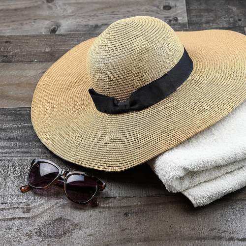 A wide-brimmed straw hat, dark sunglasses, and a white towel on a wooden surface.