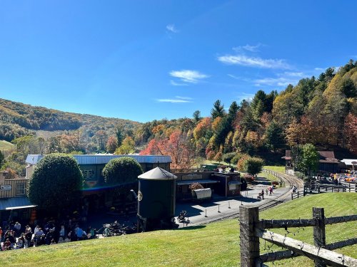 A scenic view of a vibrant autumn landscape with colorful trees, a clear blue sky, and a quaint village below.