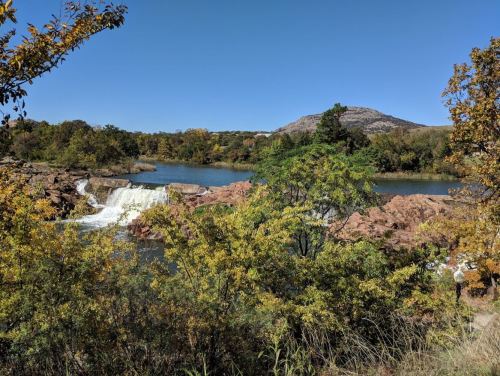 A serene landscape featuring a waterfall, a calm lake, and colorful autumn foliage under a clear blue sky.