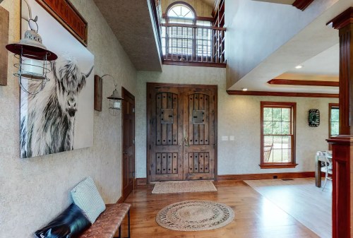 A spacious entryway with wooden doors, a bench, and a large wall art of a cow. Natural light fills the room.
